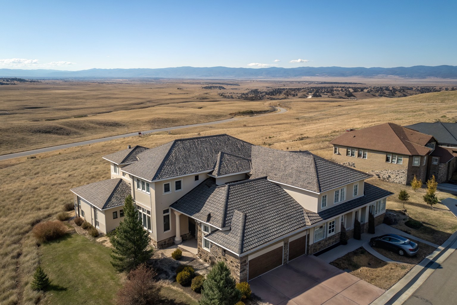 Aerial view of stucco homes with brown and gray shingle roofs on open high-plains grassland