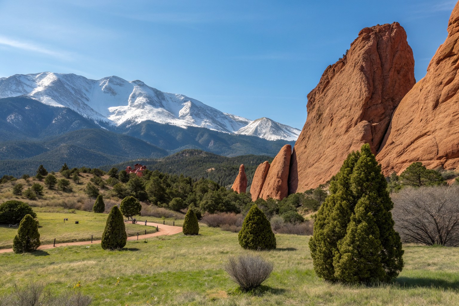 Tall red sandstone rock formations in a grassy park with a snow-capped peak behind